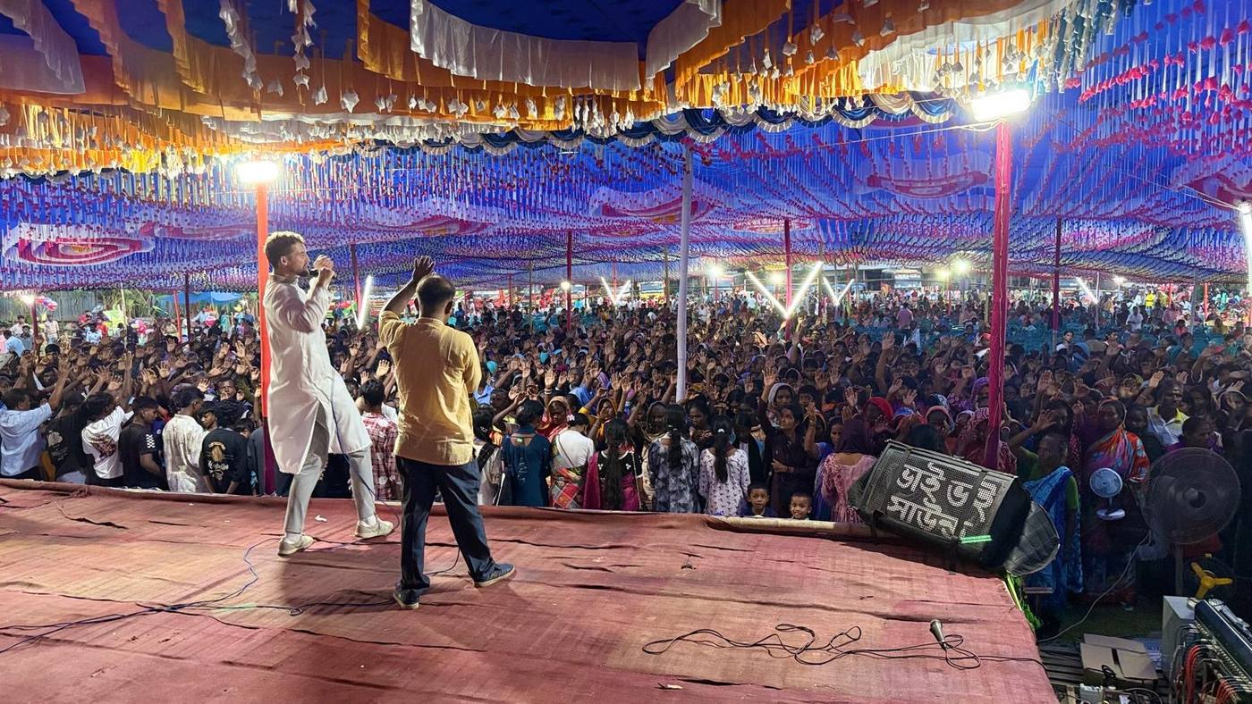 Chris preaching to a crusade crowd with hands raised in Bangladesh