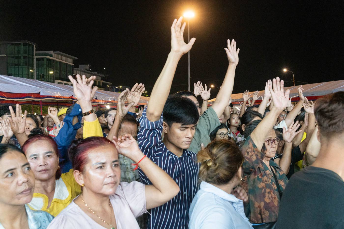 Hands raised in worship at the night crusade in Kandal, Cambodia